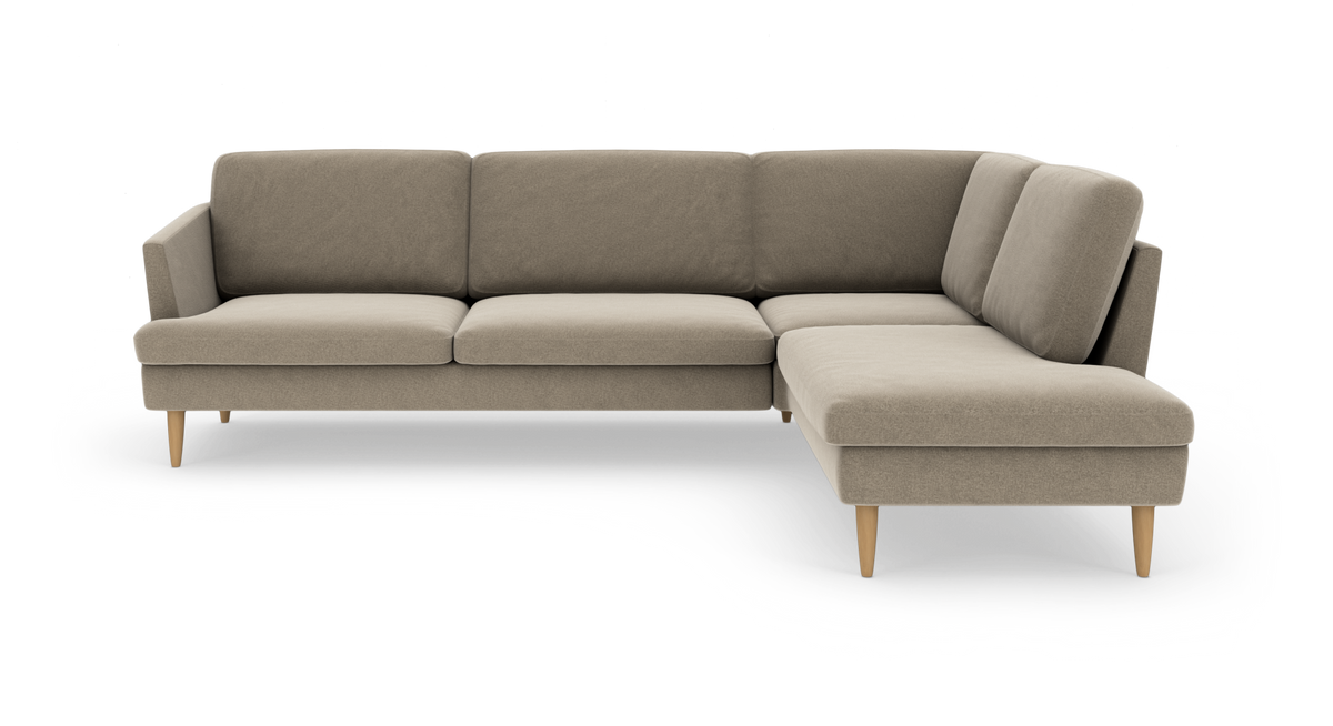 Beige L‑formet modulsofa med chaiselong til højre og lyse træben, frilagt på hvid baggrund.