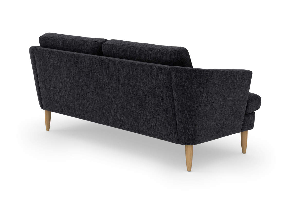 Mørkegrå stofsofa set skråt bagfra med lyse træben på hvid baggrund.