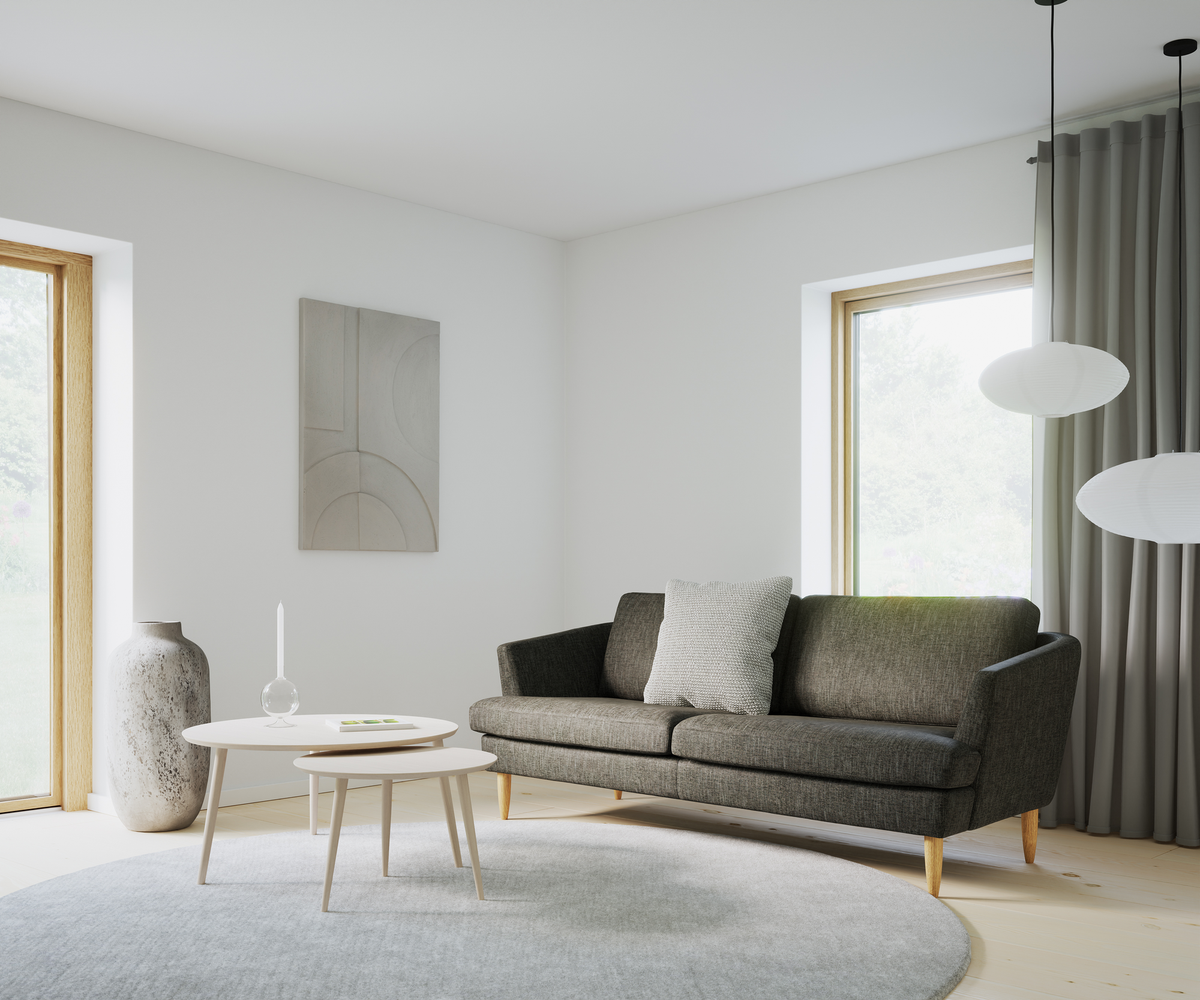 Lyst stue med mørkegrå sofa, lyse runde sofaborde, gråt tæppe, pendellamper og store vinduer med gardiner.