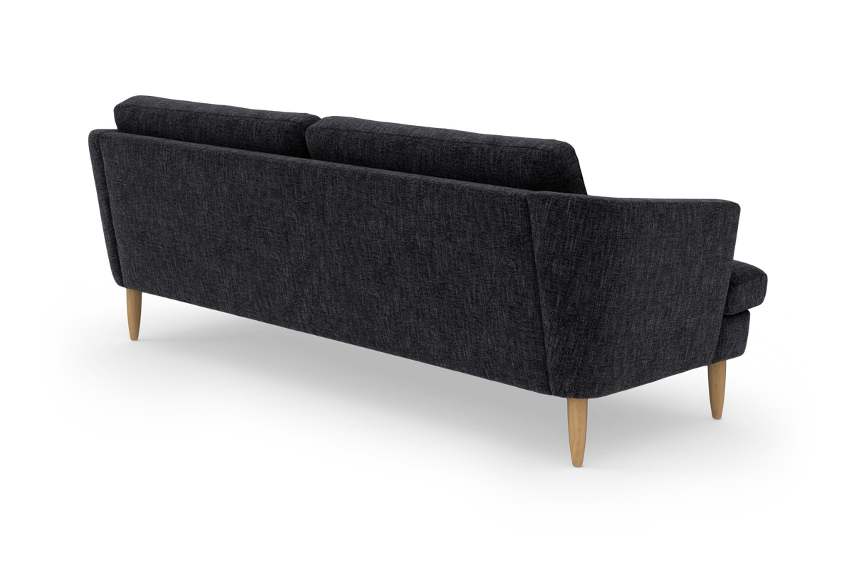 Mørkegrå sofa med slanke ben i lyst træ, set skråt bagfra i studieopsætning.