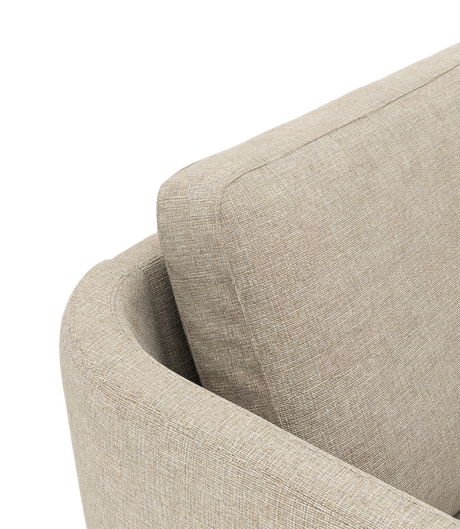 Nærbillede af beige stofsofa med afrundet armlæn og løs rygpude, fritlagt mod sort baggrund.