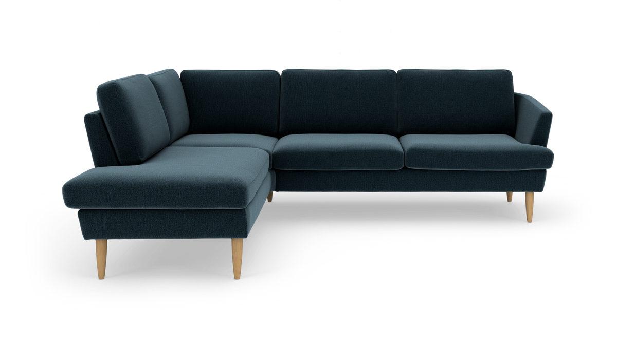 Mørk teal L‑sofa med venstrevendt chaiselong og lyse, tilspidsede træben.