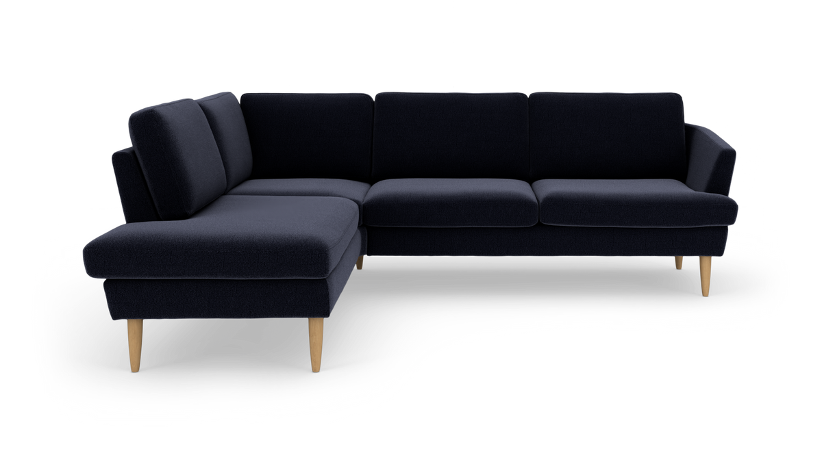 Mørkeblå L‑sofa i stof med træben, frilagt på hvid baggrund.