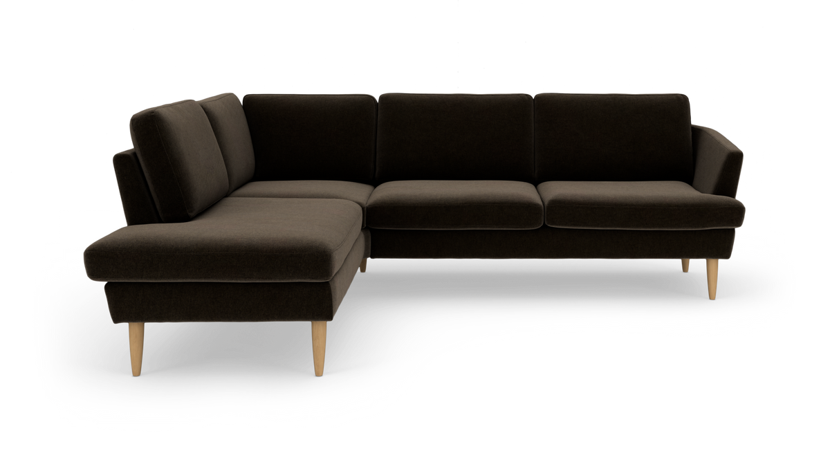 Mørkebrun L‑sofa med chaiselong til venstre, stofbetræk og tilspidsede ben i lyst træ, frilagt på hvid baggrund.