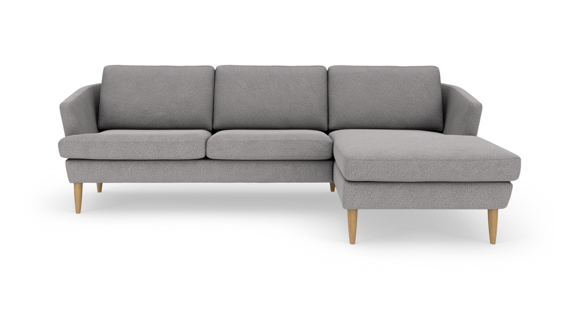 Lysegrå hjørnesofa med chaiselong i højre side og lyse træben, frilagt på hvid baggrund.