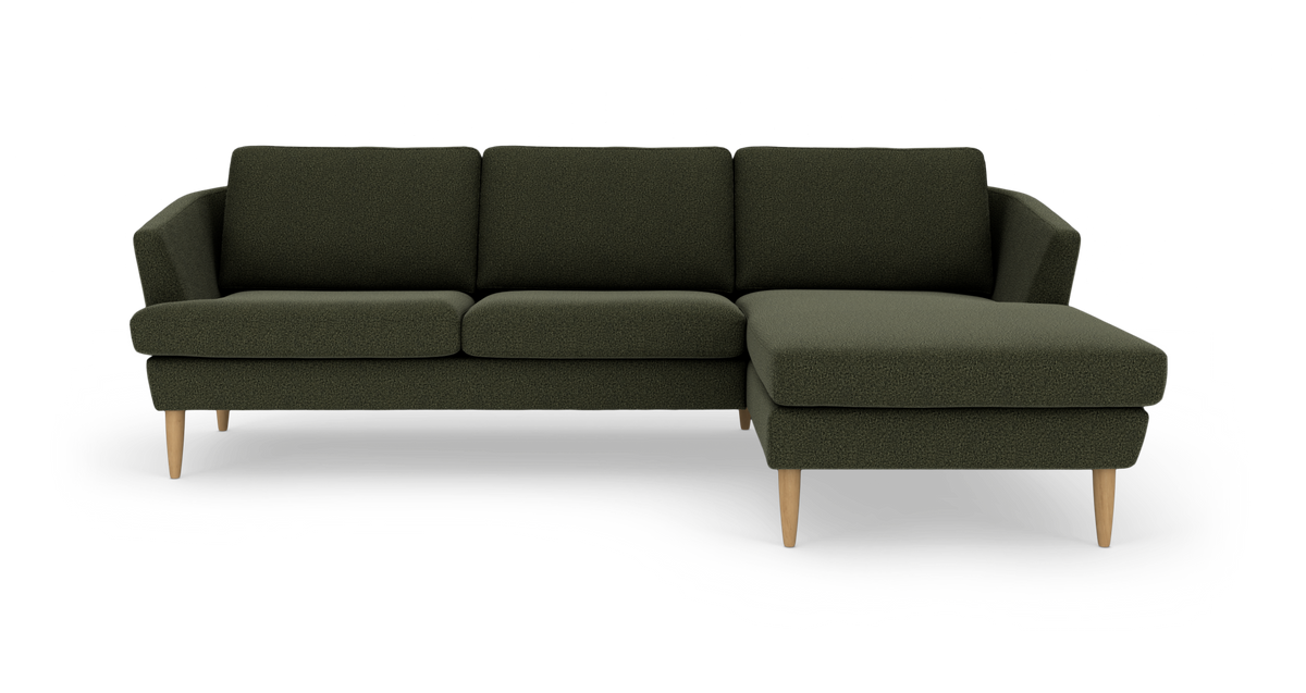 Mørkegrøn hjørnesofa med chaiselong til højre og lyse træben i studiemiljø.