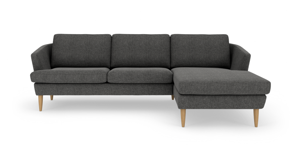 Mørkegrå hjørnesofa med chaiselong til højre og lyse træben.