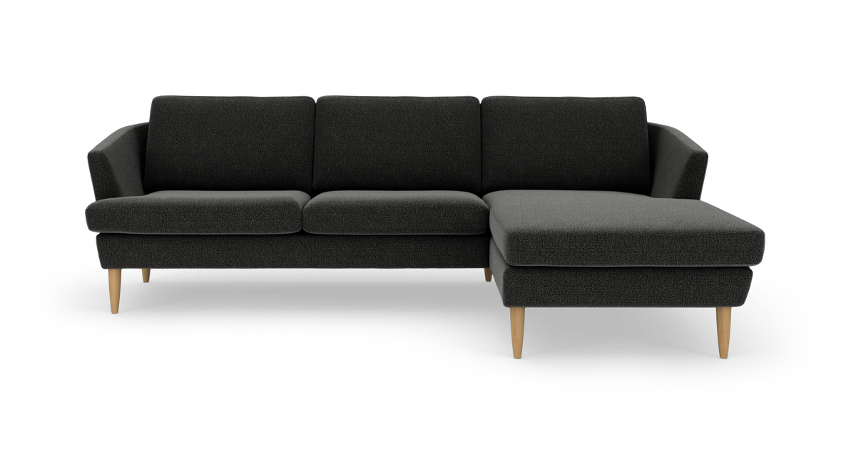 Mørkegrå hjørnesofa med chaiselong til højre og lyse træben, frilagt på hvid baggrund.