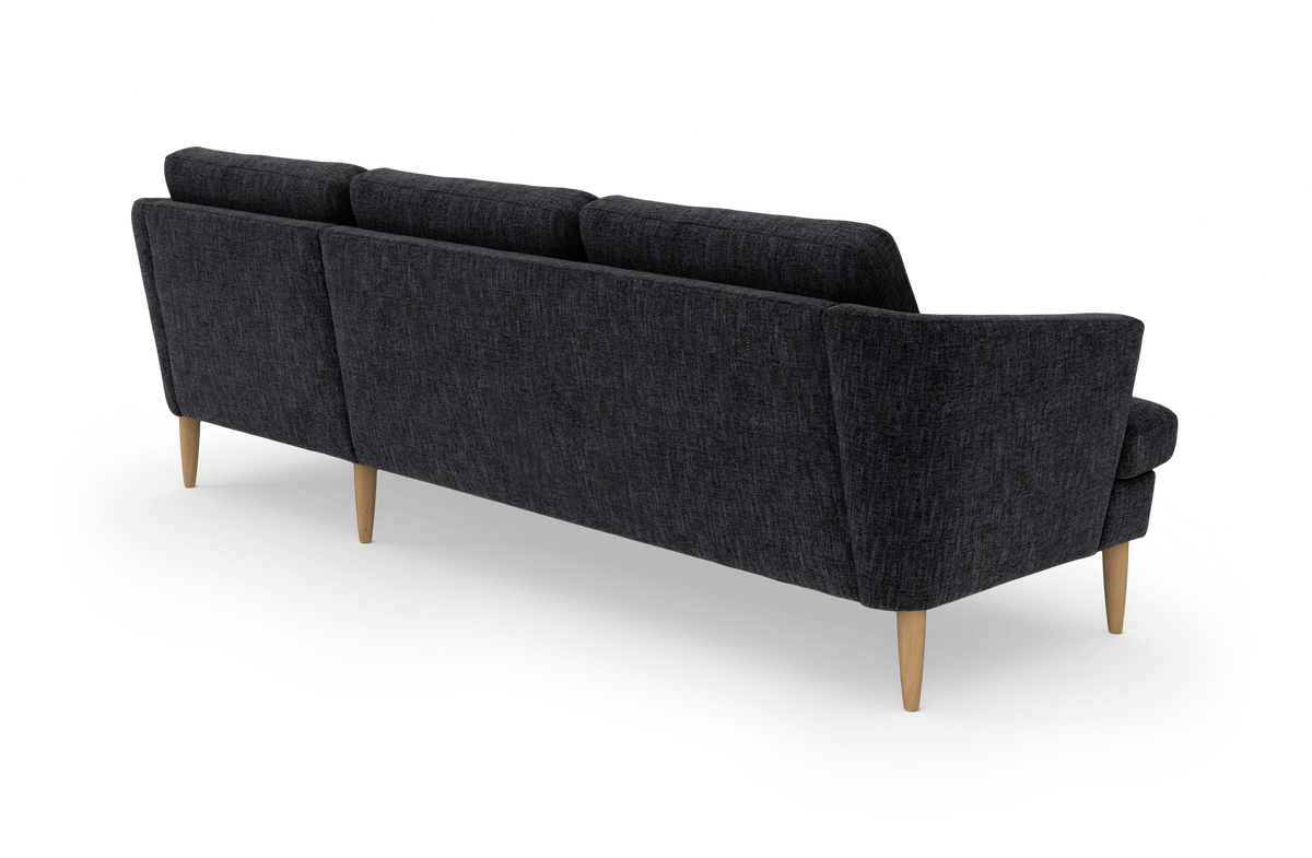 Mørkegrå tresæders sofa med træben set skråt bagfra på hvid studiebaggrund.