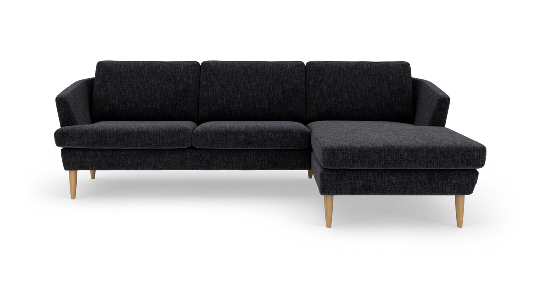 Mørkegrå hjørnesofa med chaiselong til højre og lyse træben.