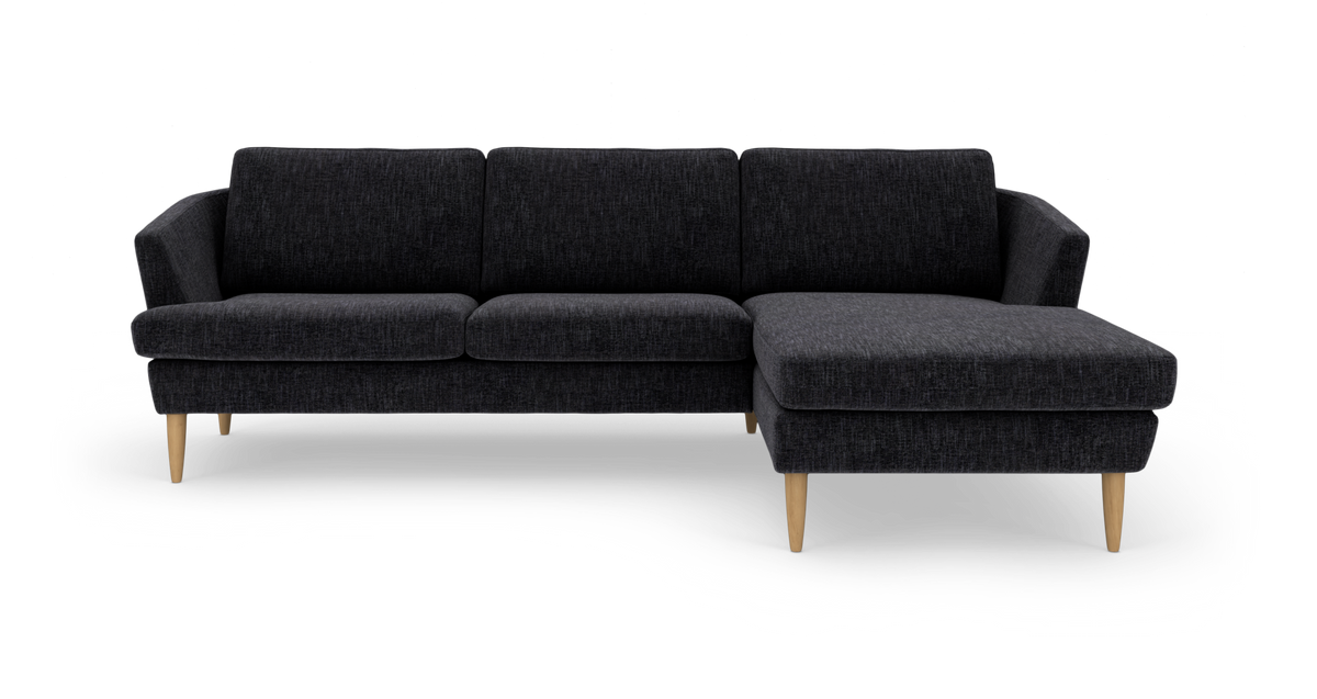 Mørkegrå hjørnesofa med chaiselong til højre og lyse træben.