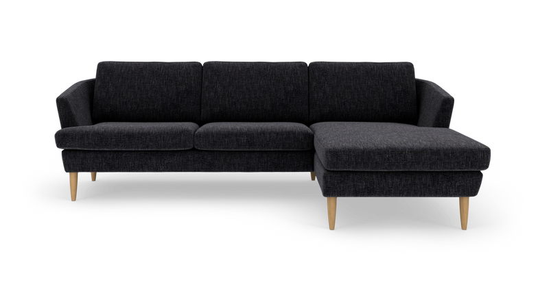 Mørkegrå hjørnesofa med chaiselong til højre og lyse træben._ps