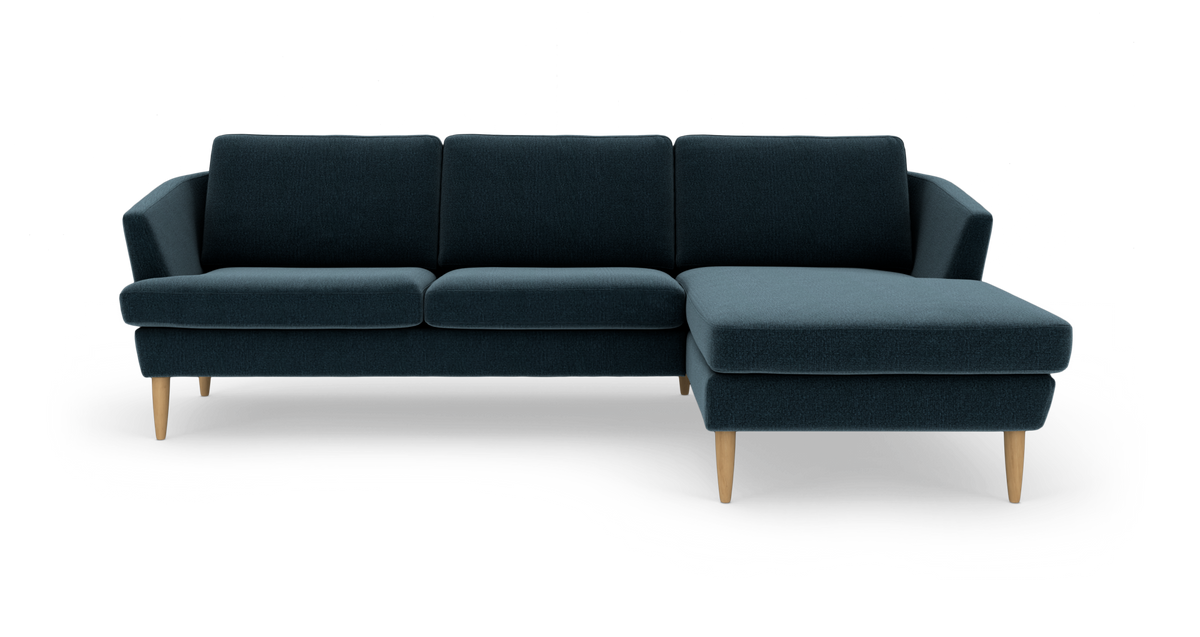 Mørkeblå hjørnesofa med chaiselong til højre og lyse træben, frilagt på hvid baggrund.