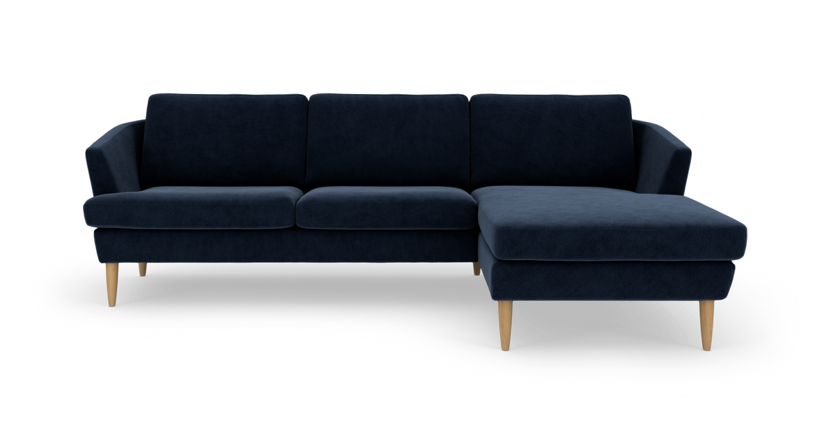 Mørkeblå hjørnesofa med chaiselong til højre og lyse træben, frilagt på hvid baggrund.