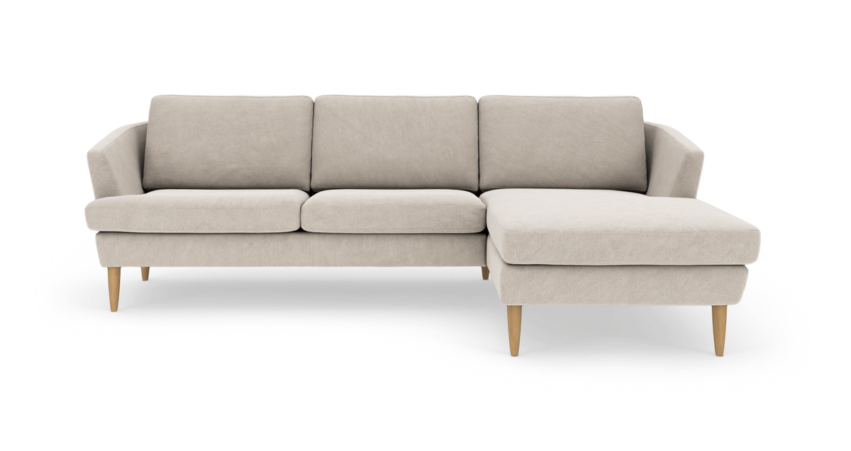 Beige hjørnesofa med chaiselong til højre og lyse træben, frilagt på hvid baggrund.