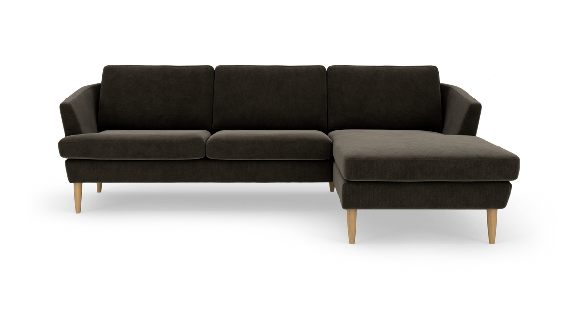 Mørk hjørnesofa med chaiselong til højre og lyse træben, frilagt mod hvid baggrund.