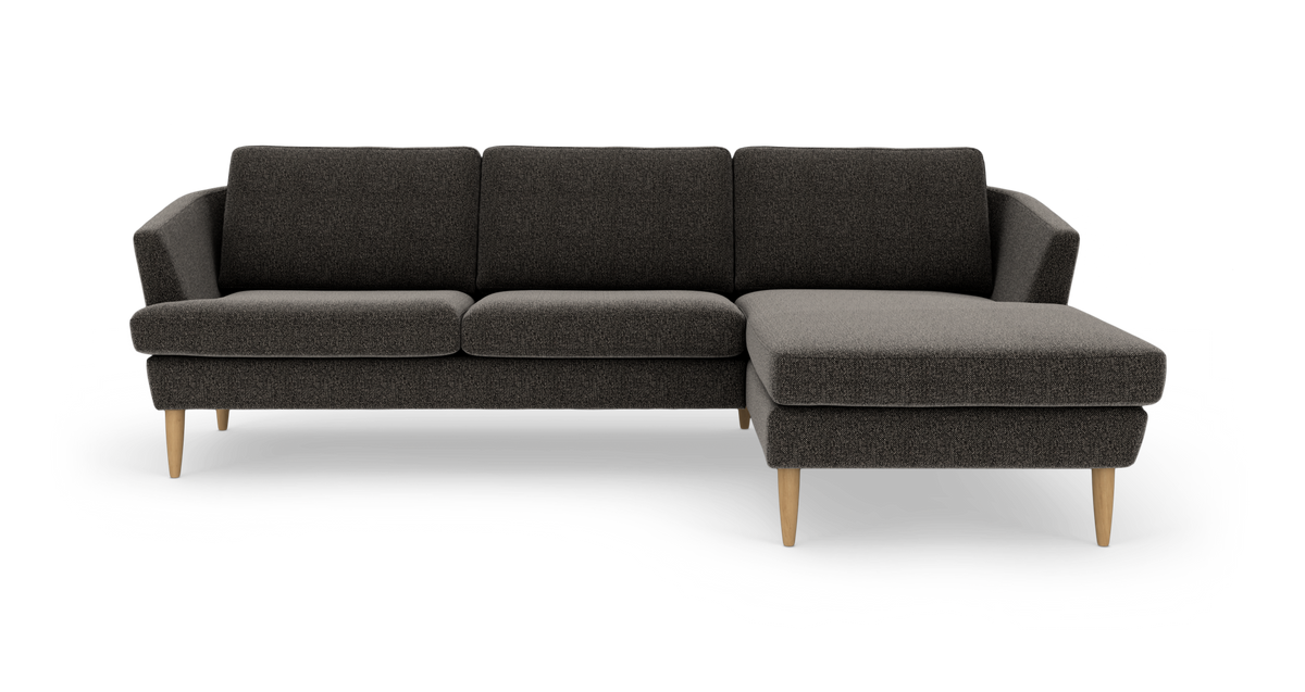 Mørkegrå hjørnesofa med chaiselong til højre og lyse træben, frilagt på hvid baggrund.