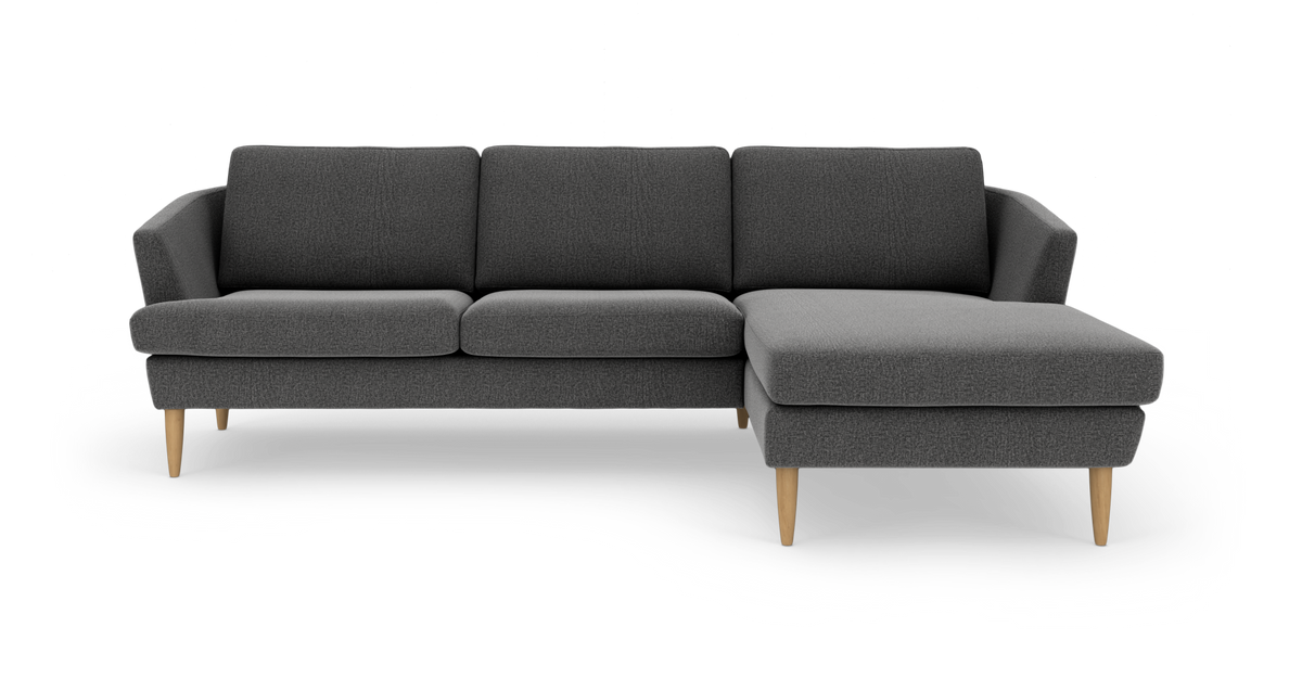 Mørkegrå modulsofa med chaiselong til højre og lyse træben, frilagt på hvid baggrund.