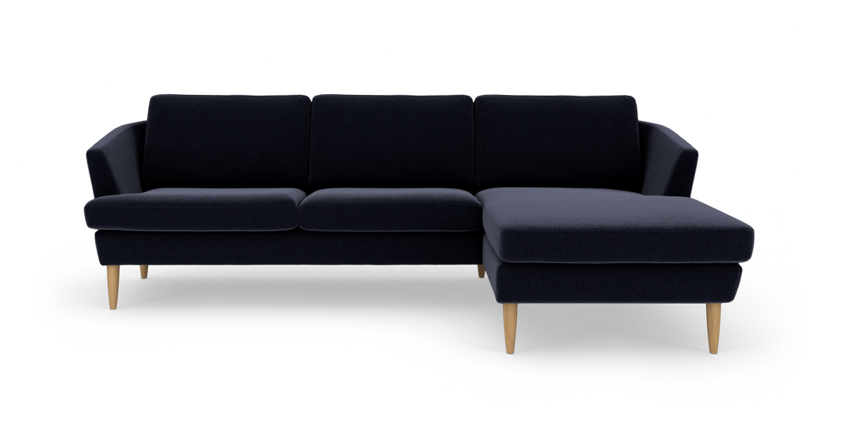 Mørkeblå modulsofa med chaiselong til højre og lyse træben, frilagt på hvid baggrund.