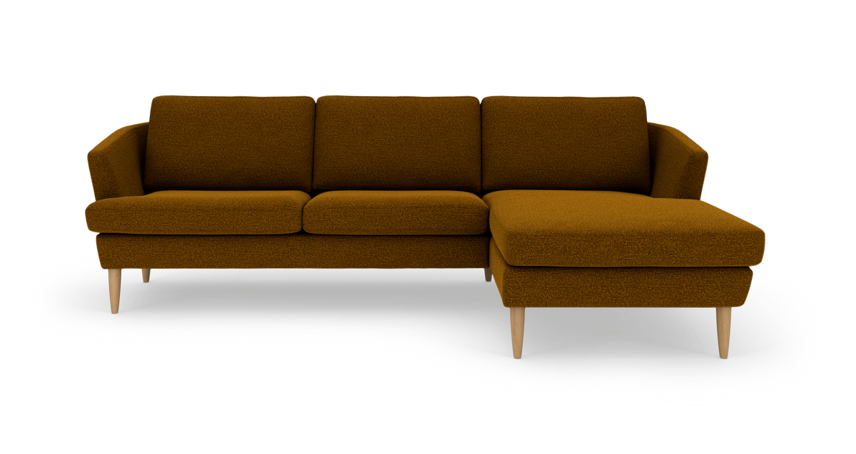 Hjørnesofa med chaiselong til højre i mørk sennepsgul bouclé og lyse træben, fritlagt produktfoto set forfra.