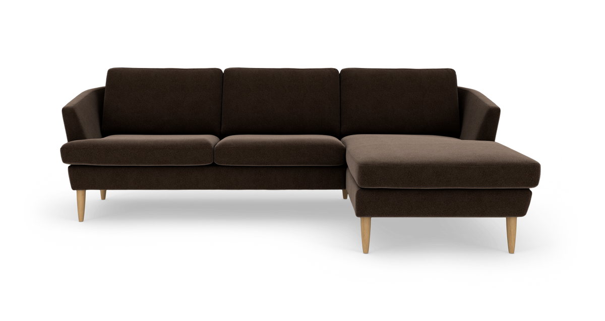 Mørkebrun hjørnesofa med chaiselong til højre og lyse træben, frontvisning isoleret på hvid baggrund.