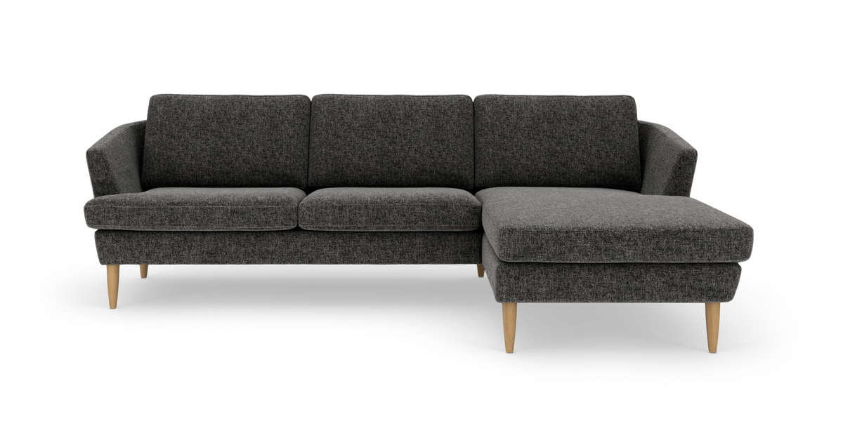 Mørkegrå hjørnesofa med chaiselong til højre, slanke træben og faste hynder på hvid baggrund.