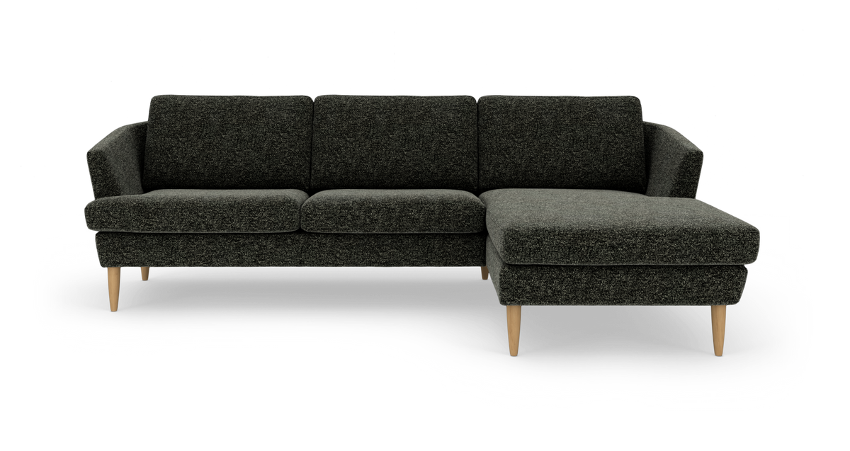Mørkegrå hjørnesofa med chaiselong til højre og koniske ben i lyst træ, fritstående på hvid baggrund.