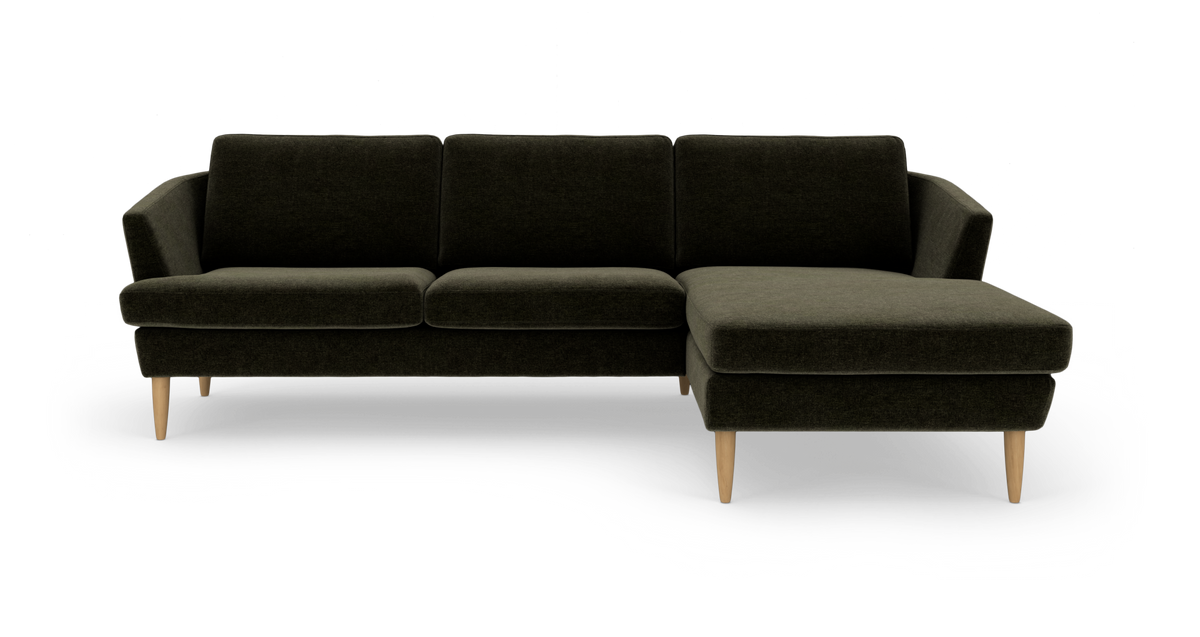 Mørkegrøn hjørnesofa med chaiselong til højre og lyse træben, frilagt produktbillede.