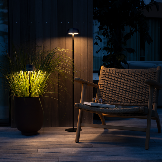Aften på terrasse med fletlænestol, gulvlampe der oplyser græs i krukke og bøger på sædet.
