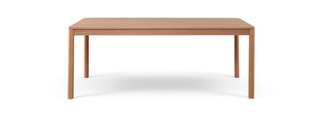 Rektangulært spisebord i lys eg med slanke runde ben, frilagt på sort baggrund.