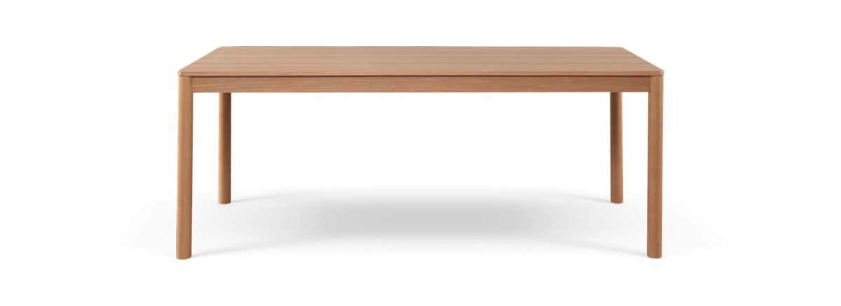 Rektangulært spisebord i lys eg med slanke runde ben, frilagt på sort baggrund.