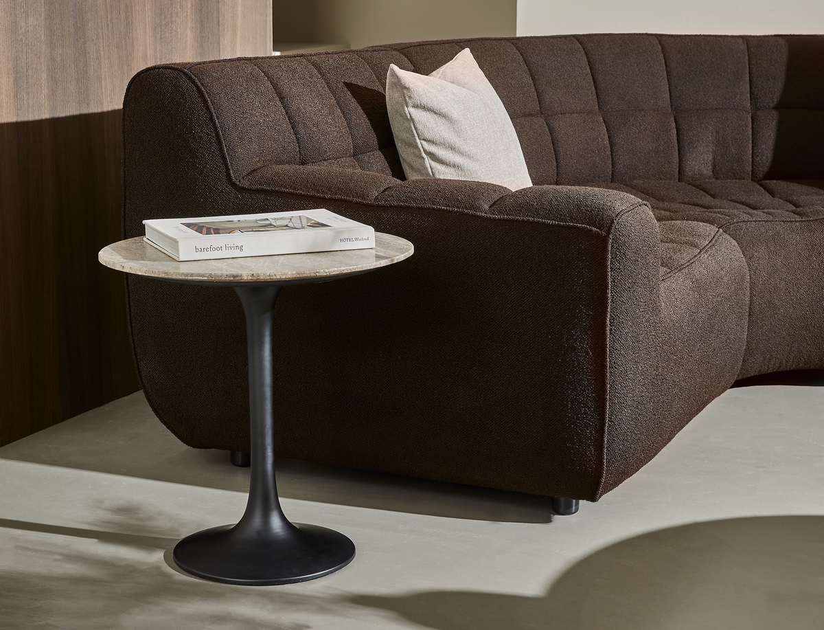 Brun tekstureret sofa med lys pude, lille rundt sidebord med stentop og sort sokkel, med bogen ”barefoot living” ovenpå.