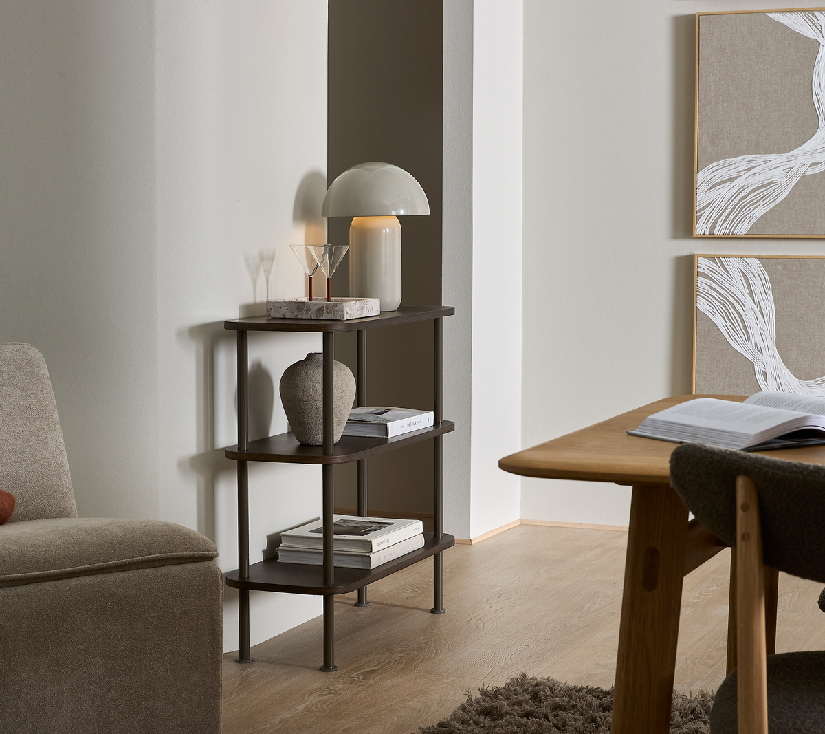 Lille mørk reol med tre hylder med bordlampe, vase og bøger; bogryg med teksten ”NORDIC”.