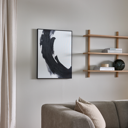 Minimalistisk stue med grå sofa, sort-hvid vægkunst og åbne træhylder med bøger som Dior og The Kinfolk samt en mørk glasvase.