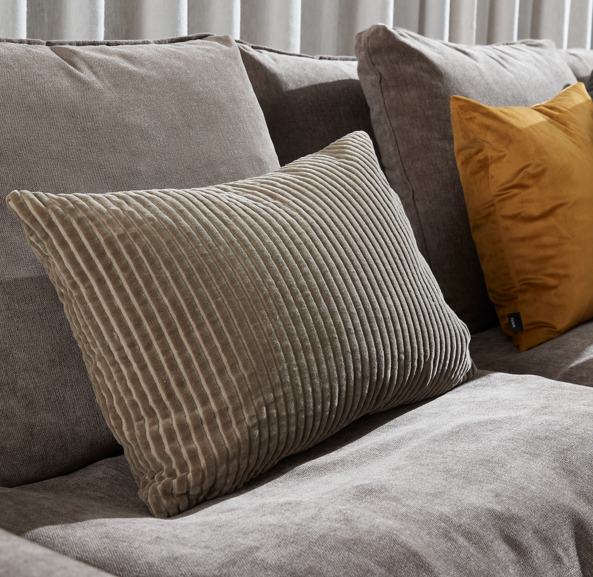 Nærbillede af grå sofa med rillet beige pyntepude og en sennepsgul pude i baggrunden.