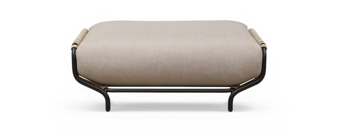Beige polstret ottoman med sort rørformet metalramme og rebdetaljer på enderne, fritlagt mod sort baggrund, set lige forfra.