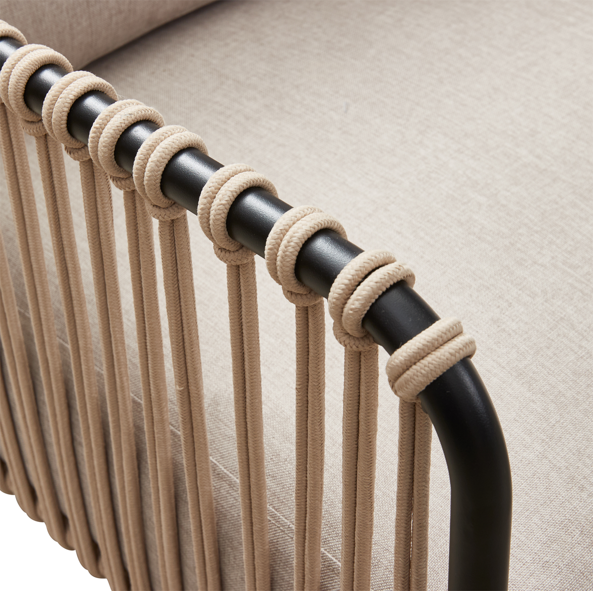 Nærbillede af en stol med sort, rund metalramme, hvor armlænet er viklet med beige snor, med beige tekstilbaggrund.