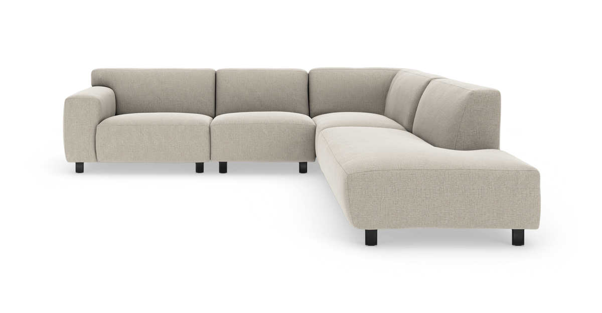 Lys beige modulsofa i L‑form med bred chaiselong, bløde afrundede armlæn og sorte ben.