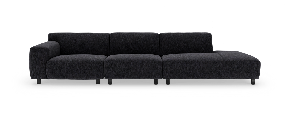 Modulsofa i mørkegråt stof med venstre armlæn og chaiselong til højre, fotograferet forfra mod hvid baggrund.