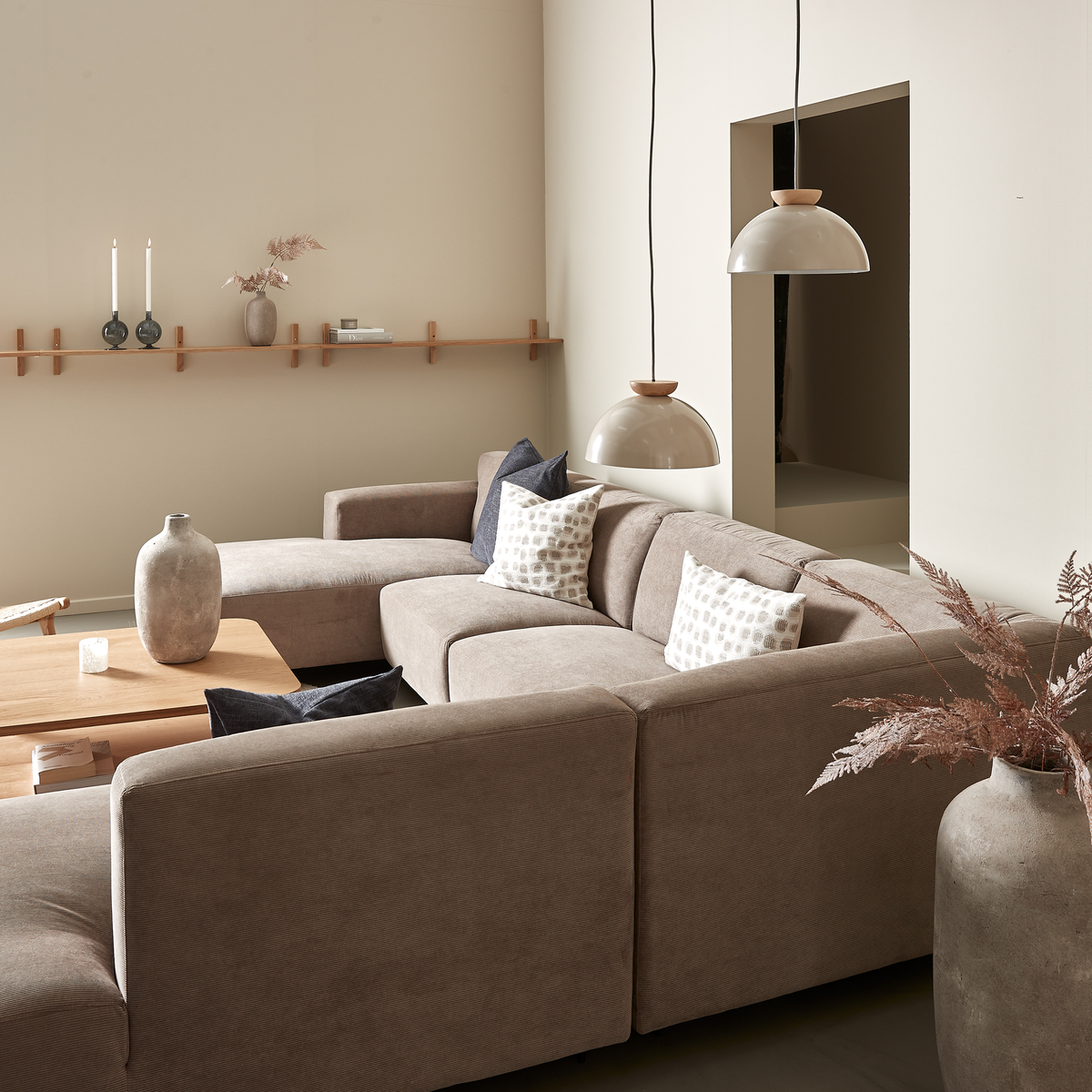 Beige stue med modulsofa, træbord, to kuppelformede pendler og keramikvaser i neutrale nuancer.