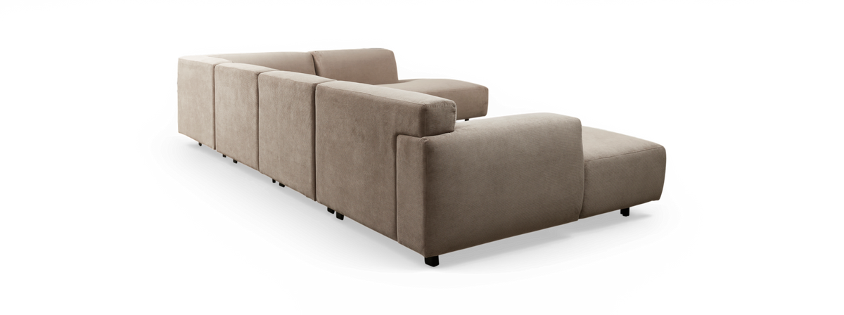 Beige modulsofa i stof set skråt bagfra mod sort baggrund.