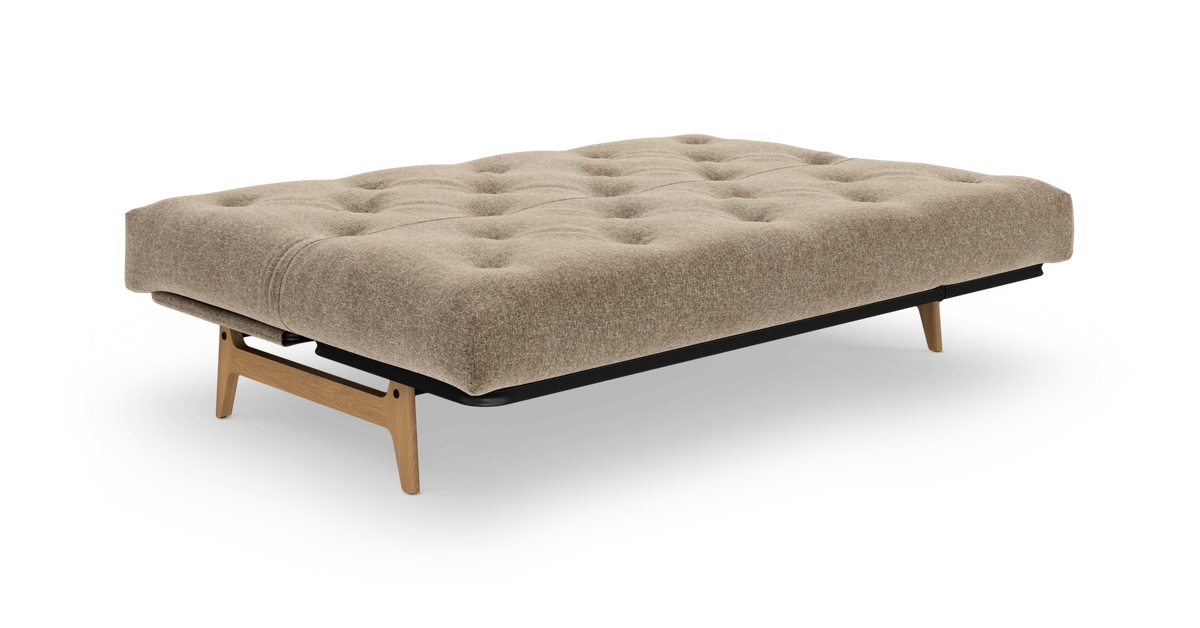 Beige, tuftet sovesofa med træben på hvid baggrund.