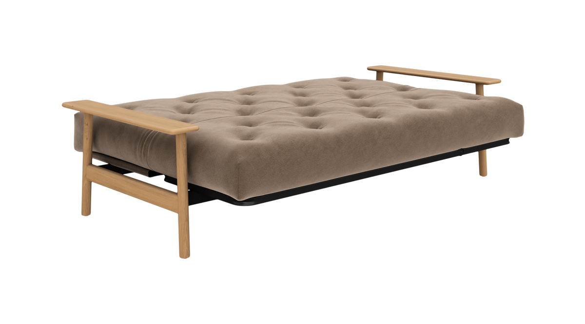 Beige, tuftet sovesofa/futon med lyse træarmlæn, frilagt på hvid baggrund i frontvinkel.