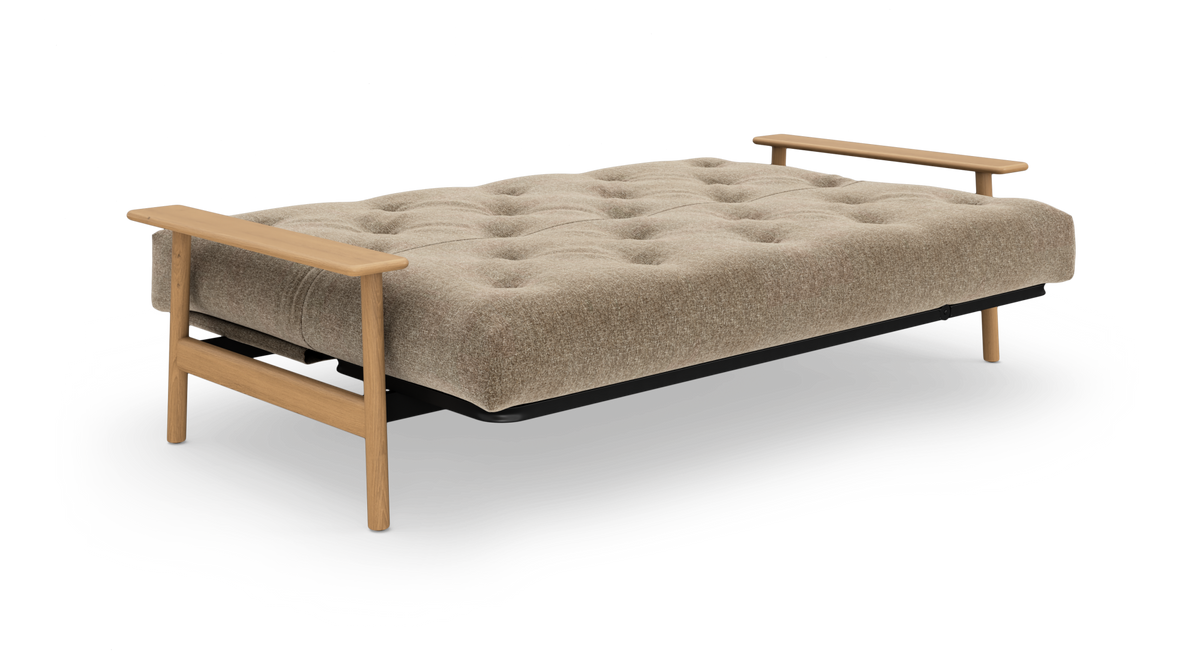 Beige sovesofa med tuftet madras og træarmstøtter, frilagt på hvid baggrund.