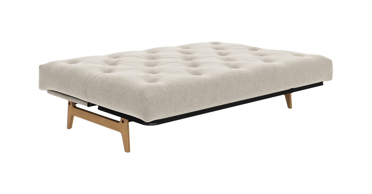 Beige sovesofa i udslået position med tuftet madras og træben, frilagt på hvid baggrund.
