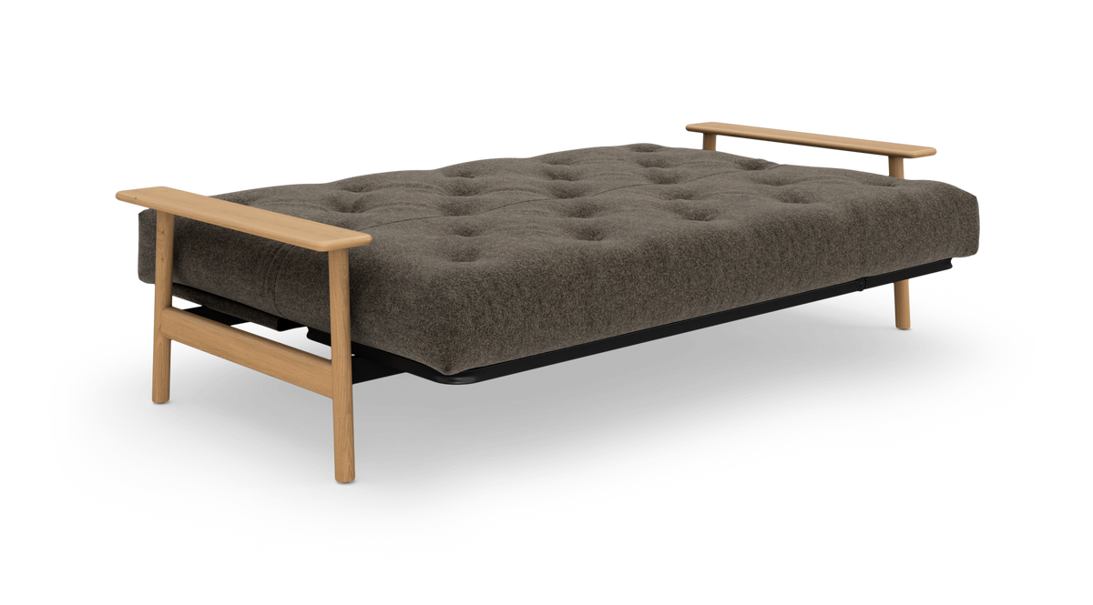 Sovesofa lagt helt ned med tuftet gråbrun madras, sort ram og lyse træarmlæn og ben, frilagt på hvid baggrund.