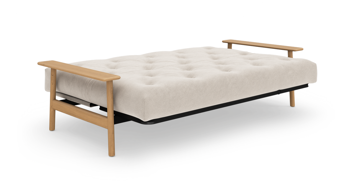 Beige sovesofa i udslået position med tuftet madras, sort ram og lyse træarmlæn.