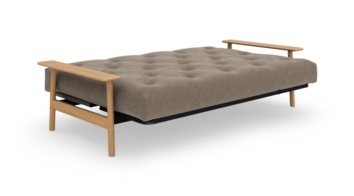 Beige sovesofa med tuftet madras og lyse træarmlæn, fritstående på hvid baggrund.