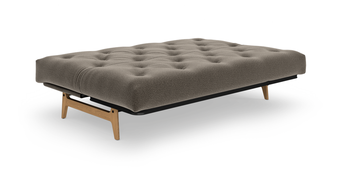 Beige/grå tuftet futon/sovesofa med træben, frilagt på hvid baggrund.