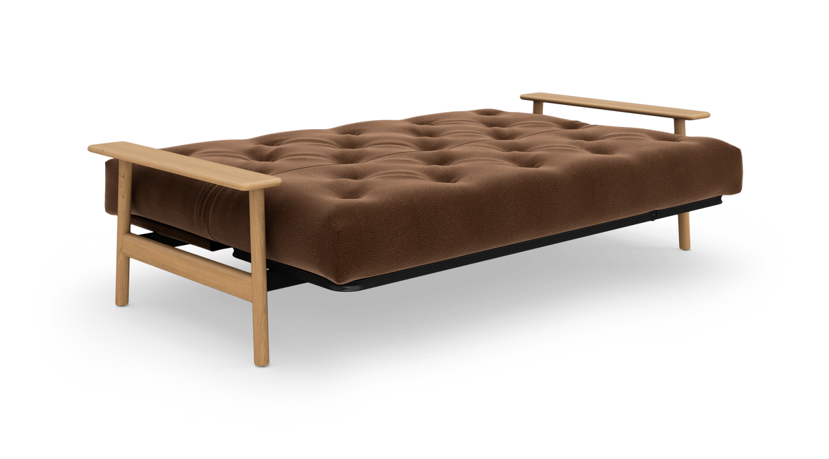 Brun, tuftet sovesofa med lyse træarmlæn og ben, frilagt på hvid baggrund.